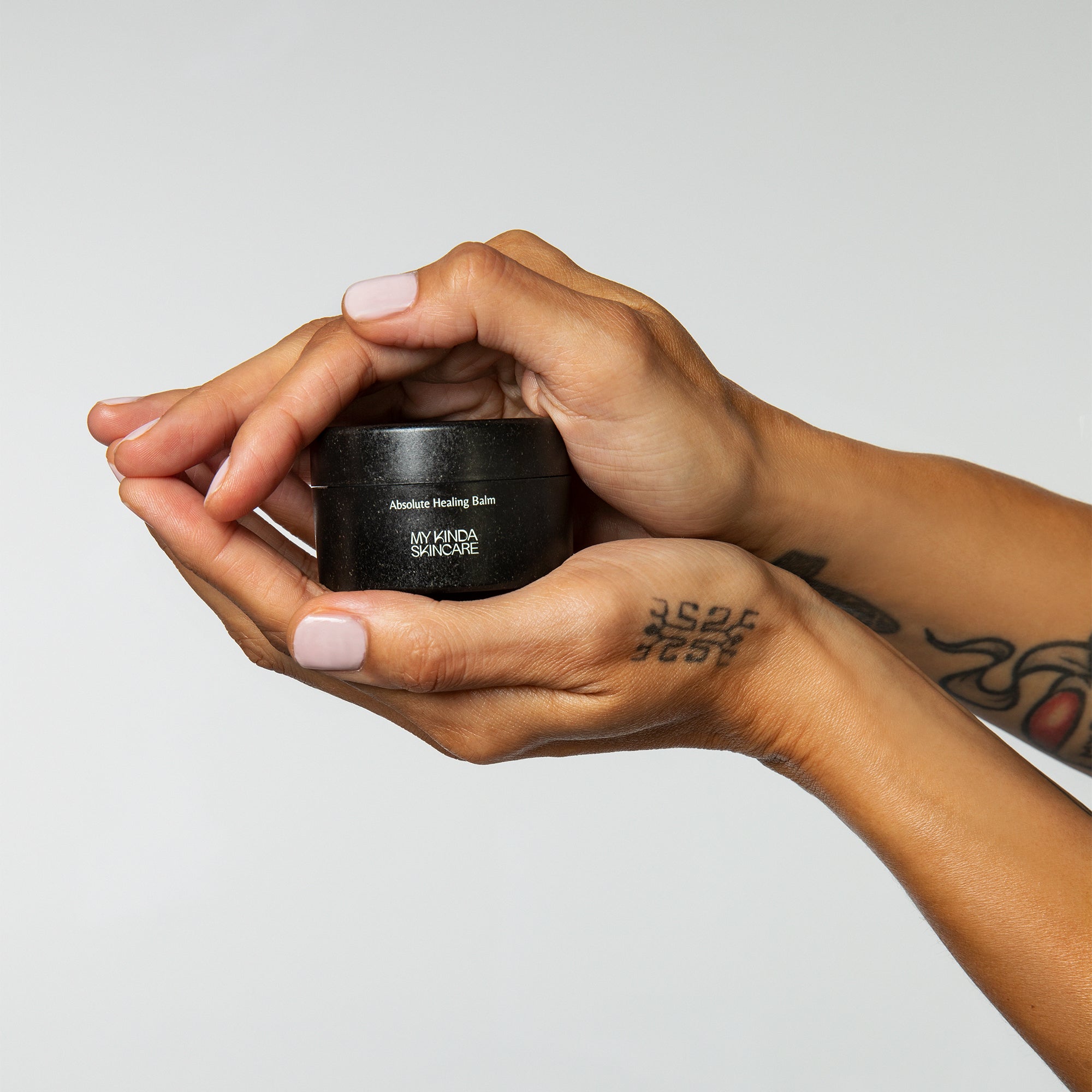 Handen houden een My Kinda Skincare potje vast – een rijke sheaboter balm in duurzame verpakking. De geurloze balm met alleen essentiele ingredienten die goed zijn voor de huid voedt en verzorgt handen, nagels en tattoo.